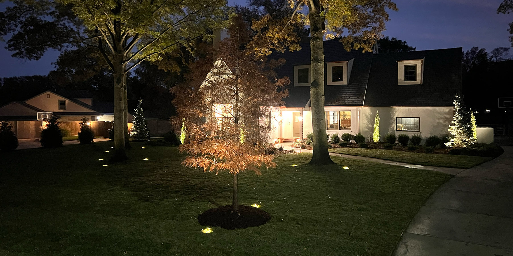 Front elevation of white brick home at night with lights.