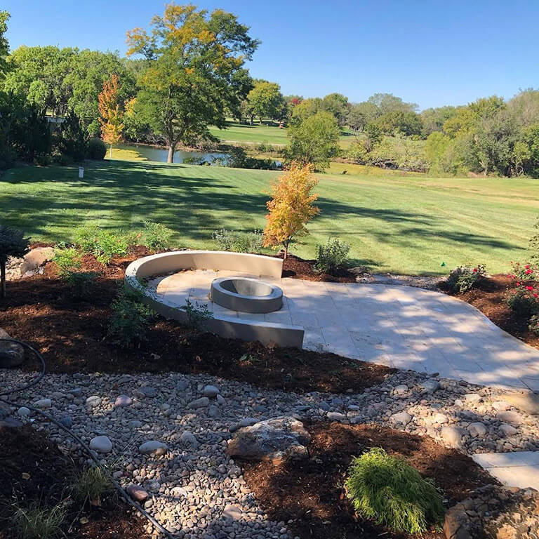 A patio with fire pit overlooking a lush lawn.