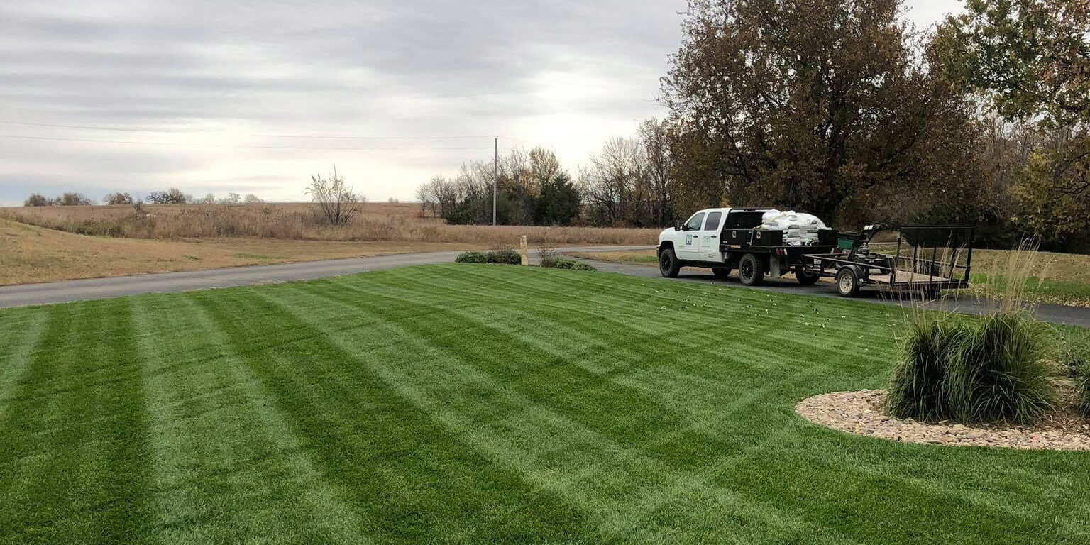 The High Caliber Landscape truck sits in the distance beyond a green lawn.