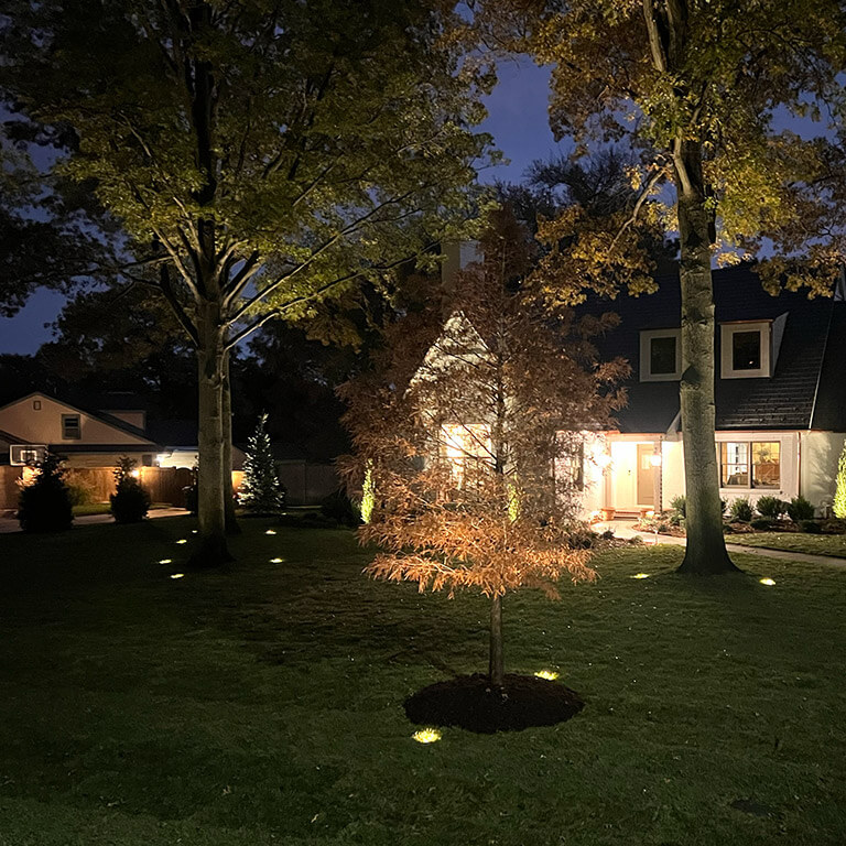 Front view of a home at night with landscape lighting.