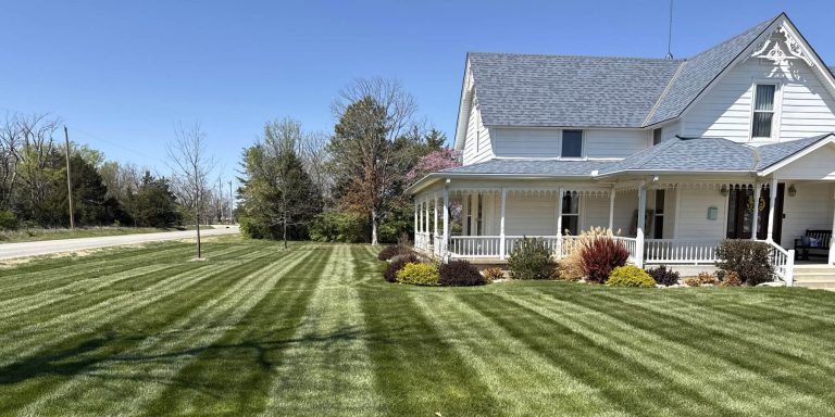 A neatly maintained lawn with stripes with a white farm house.