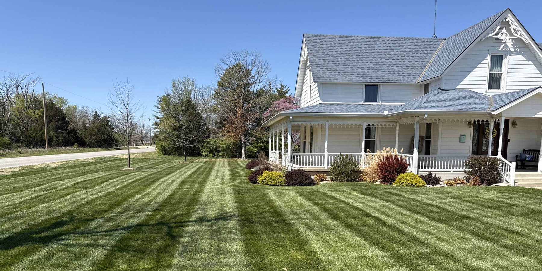 A neatly maintained lawn with stripes with a white farm house.
