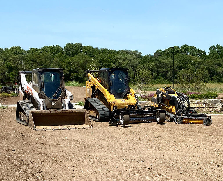 Two track loaders and a mulcher sit on a dirt lot.