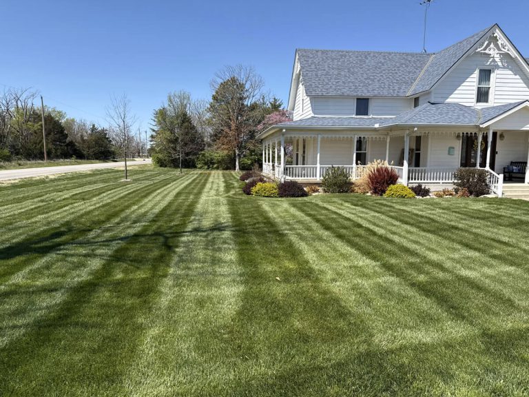 A neatly manicured lawn with stripes with a white farm house.