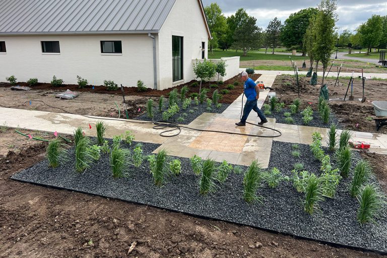 A High Caliber Landscape expert maintains a garden bed of plants.
