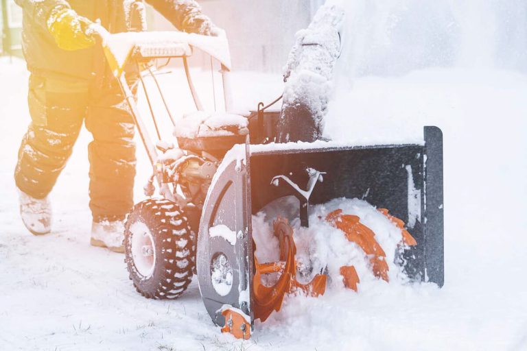An unseen person pushes a snow blower.
