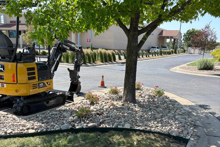 A landscaped rock bed surrounds a tree in the Walgreens parking lot. Heavy equipment is in the foreground.